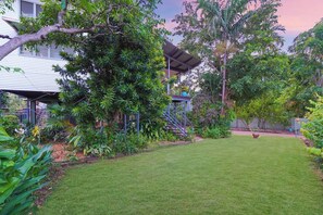 A backyard with a lawn, a covered patio, and various plants.