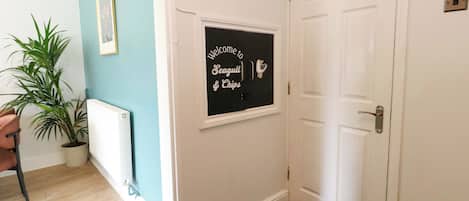 A hallway with a door, a framed welcome sign, a potted plant, and a radiator.