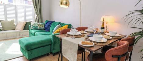 A dining area with a table set for two, a sofa, and a lamp.
