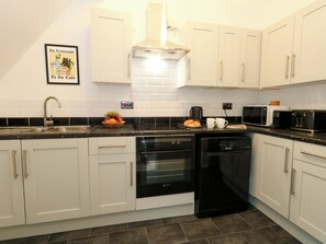 A modern kitchen with white cabinets, a black countertop, a dishwasher, an oven, a microwave, and a coffee maker. - Seagull and Chips (Weymouth)