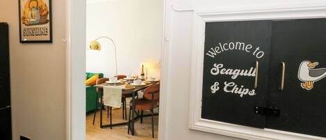 Un comedor con una mesa lista para cuatro personas, un sofá verde y un ventilador de techo.