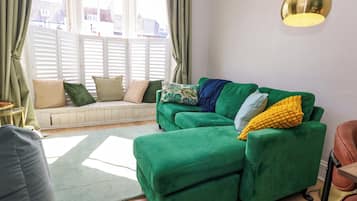 A green sofa with a bench, a round table, and a lamp.