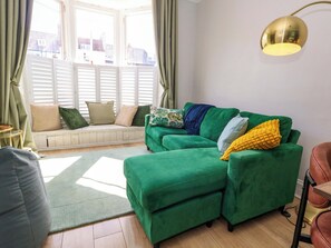 A green sofa with a bench, a round table, and a lamp.