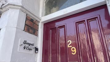Una puerta roja con el número 29, un timbre blanco y un cartel que dice 'Seagulls & Chips' en la pared.