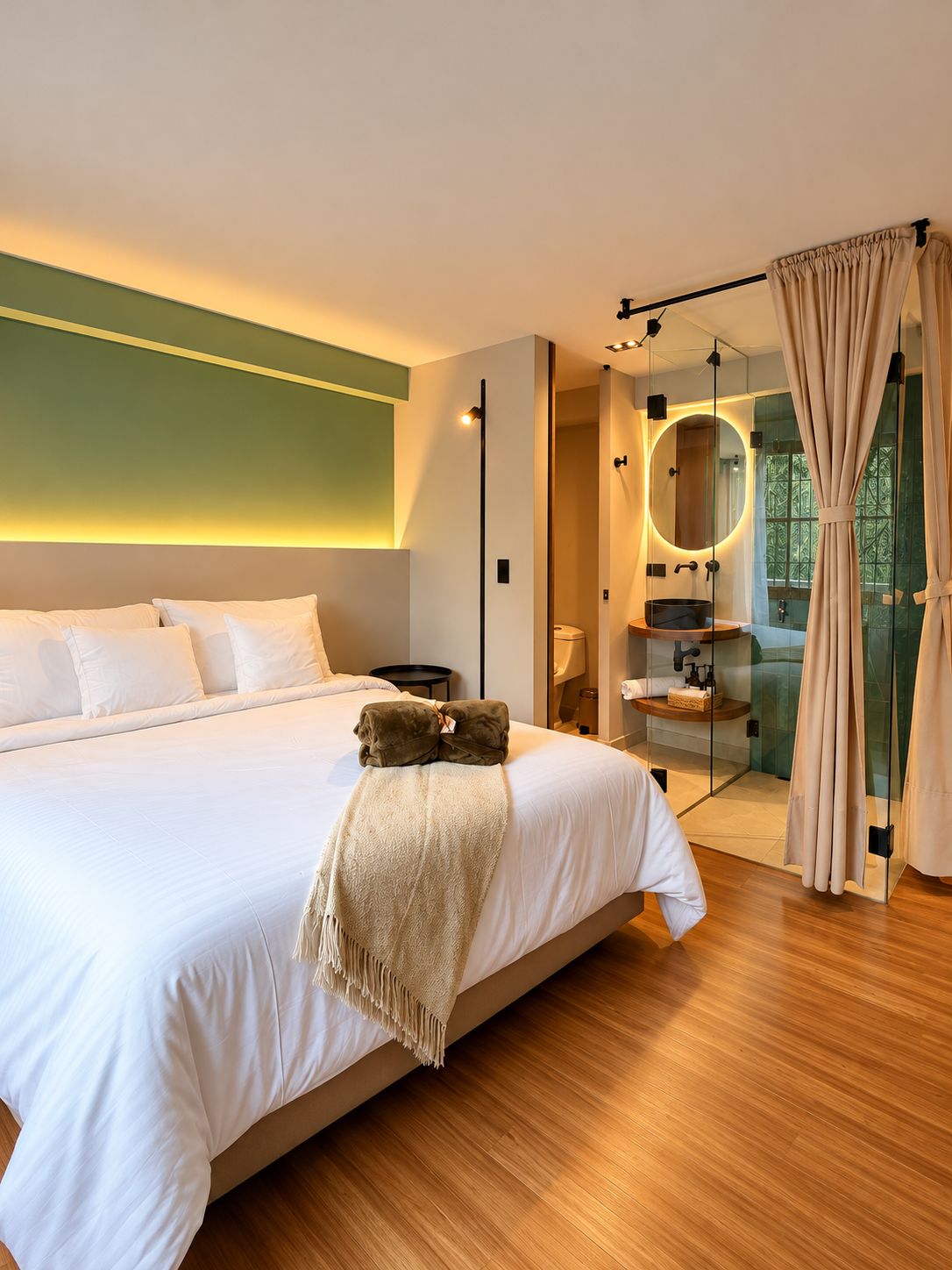 Une chambre moderne avec un grand lit, une salle de bain fermée par des parois de verre et une vue sur la verdure environnante.