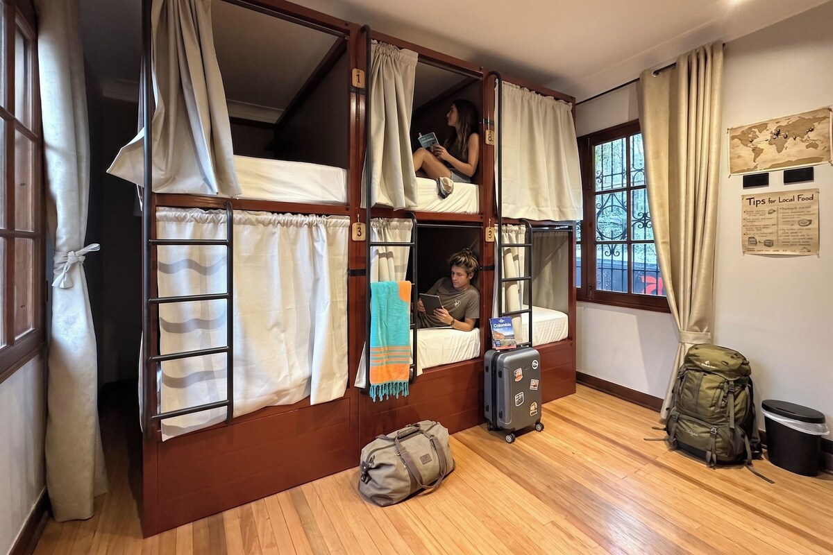 A dormitory room with bunk beds, a suitcase, and a backpack.