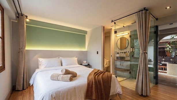 A modern bedroom with a large bed, a glass shower enclosure, and a view of the outdoors. - Sereno Hostels (Bogota)