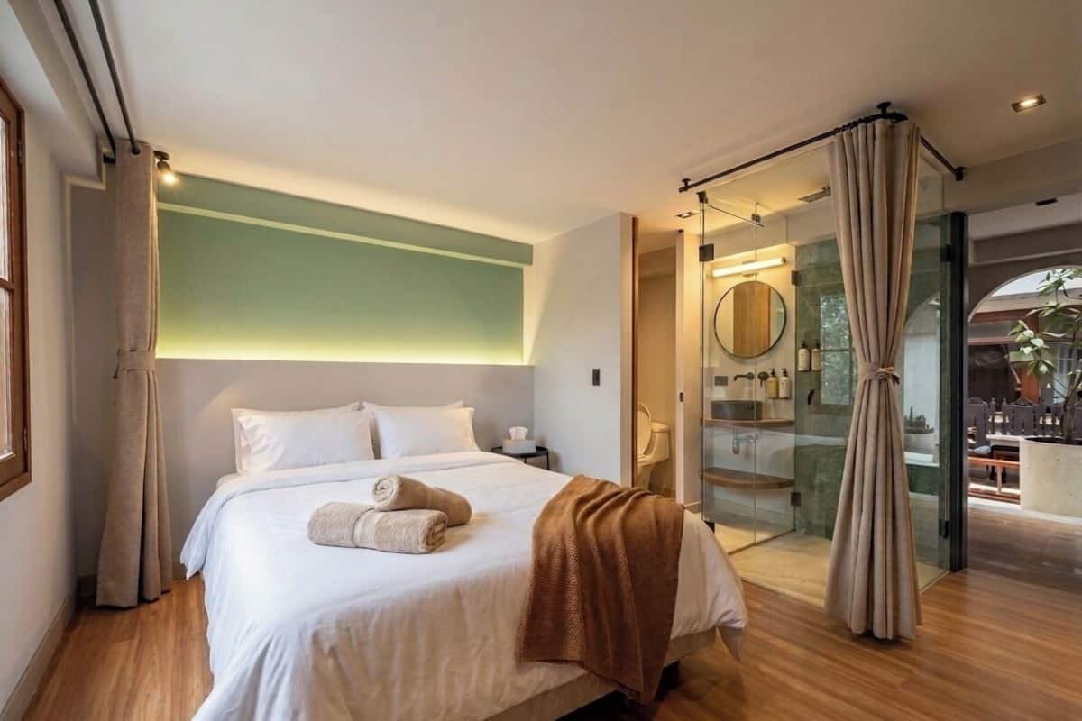 A modern bedroom with a large bed, a glass shower enclosure, and a view of the outdoors.