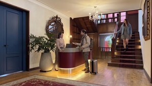 A reception area with a desk, a large potted plant, a red carpet, and a staircase. - Sereno Hostels (Bogota)