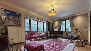 A room with a grand piano, a red sofa, a bench, and a laptop on a table. - Sereno Hostels (Bogota)