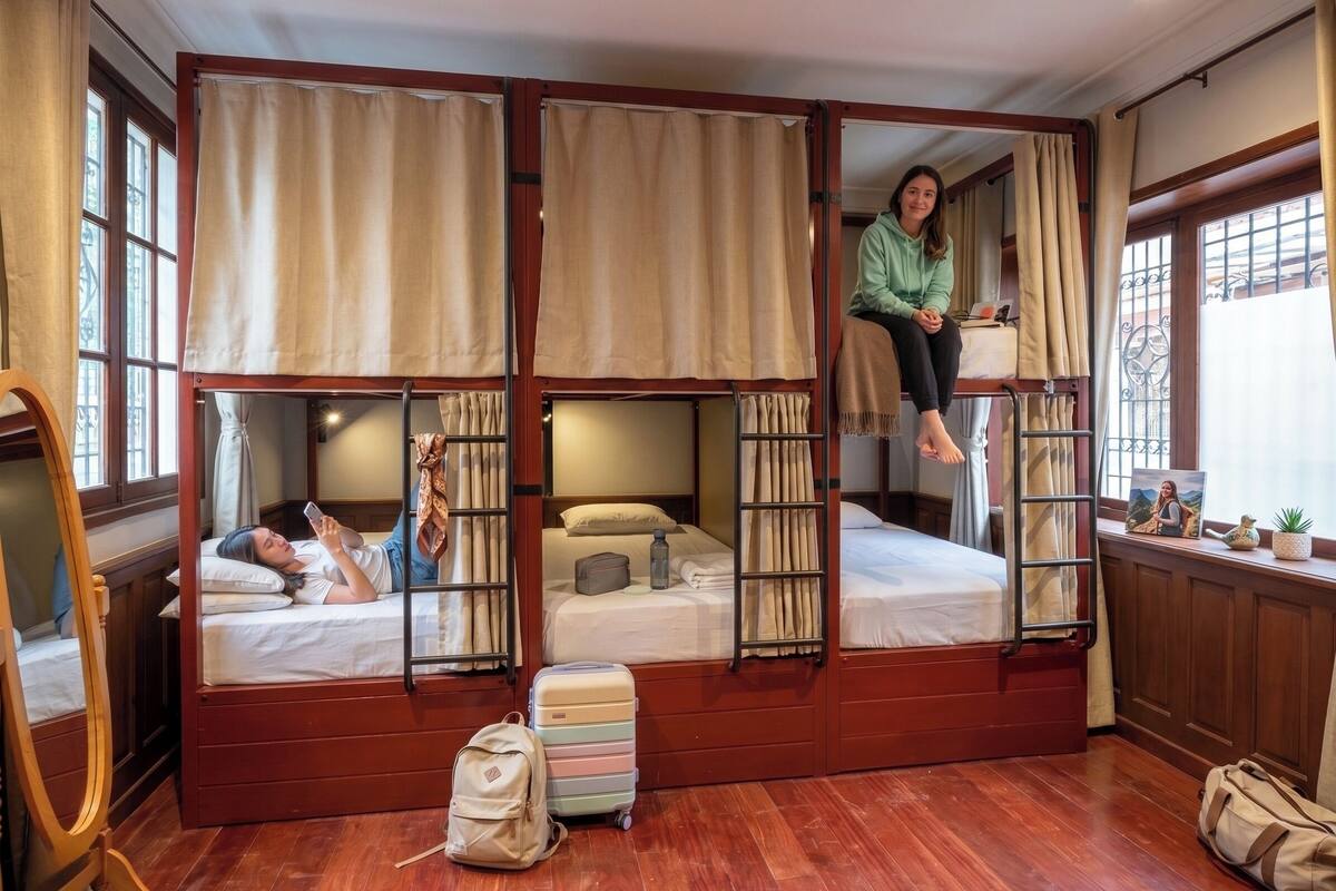 A bunk bed room with a wooden floor, a small table, and a window with curtains.