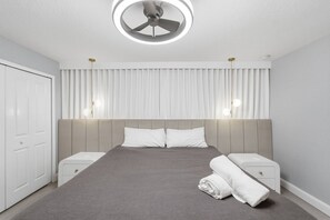 Ein modernes Schlafzimmer mit Bett, Nachttischen, Deckenventilator und einem Fenster mit Vorhängen.