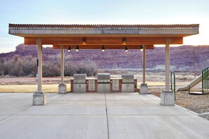 An outdoor barbecue area with a wooden pergola, three grills, and a playground slide. - EBAC Moab (Moab)