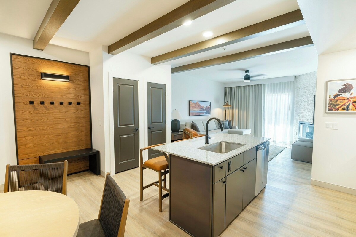 A modern kitchen with a central island, wooden panel wall, and a dining area with chairs.