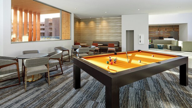 A modern living room with a pool table, comfortable seating, and a large window offering a view of the cityscape.