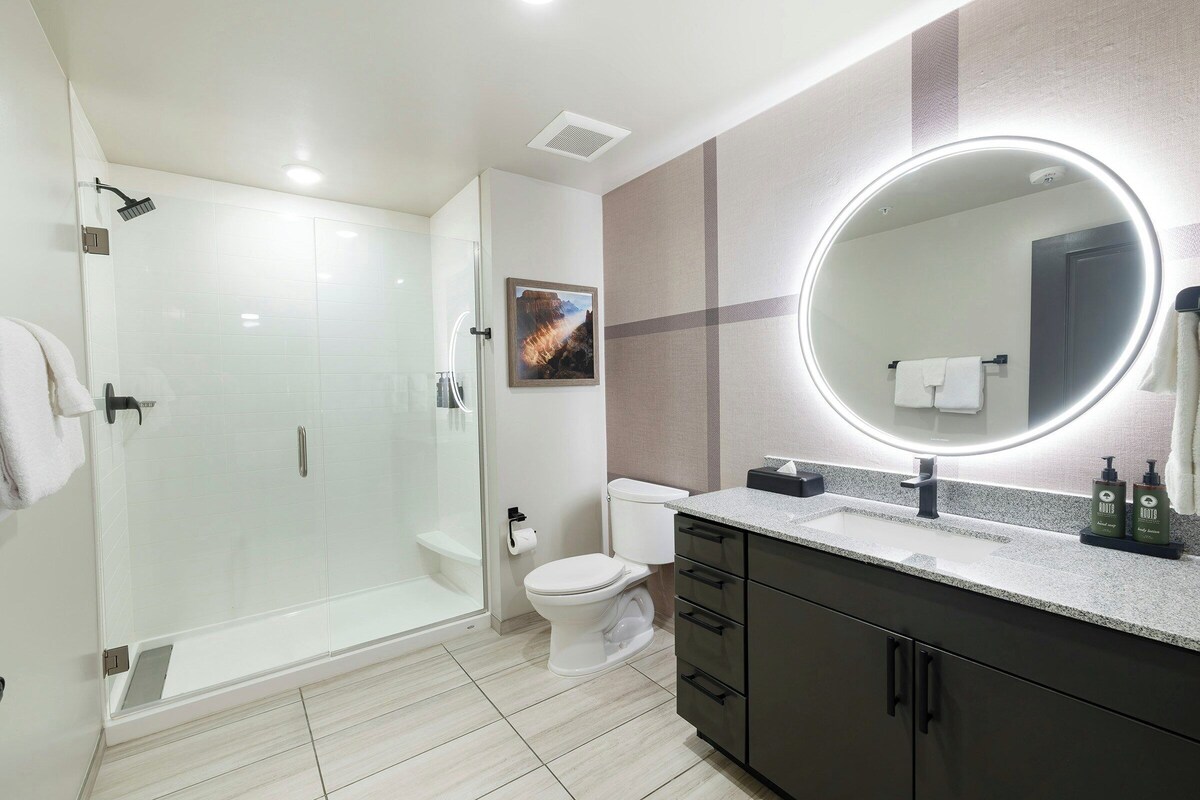 A modern bathroom with a glass-enclosed shower, a toilet, a vanity with a mirror, and a sink.