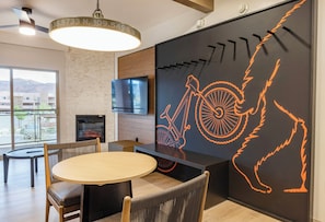 A modern interior with a round dining table, chairs, a flat-screen TV, a fireplace, and a wall with a bicycle and abstract art. - EBAC Moab (Moab)