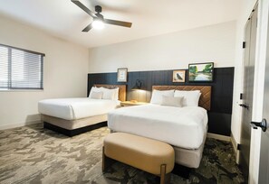A hotel room with two beds, a bench, a ceiling fan, a nightstand, and a window with blinds. - EBAC Moab (Moab)