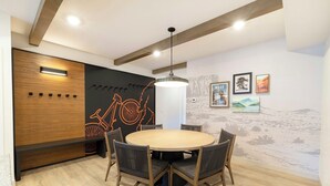 A conference room with a round table, six chairs, a wooden accent wall, a wall-mounted light fixture, and framed artwork.
