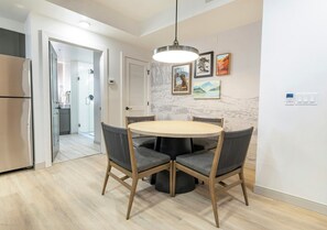 Ett modernt kök med ett inbyggt kylskåp, en matplats med ett runt bord och fyra stolar samt en hall som leder till ett badrum.