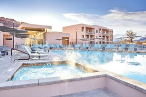 A pool area with lounge chairs, a hot tub, and a building with balconies. - EBAC Moab (Moab)