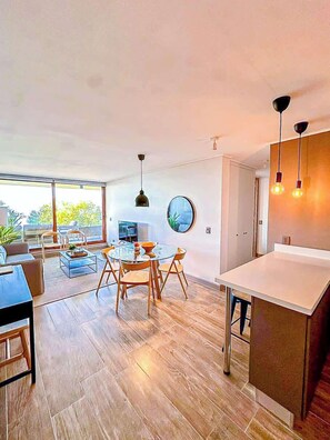 A modern living room with a dining area, large windows, and a view of greenery.