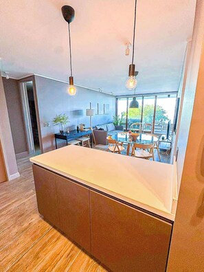 A modern kitchen with a large island, pendant lighting, and a view of the outdoor dining area.