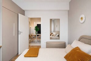 Ein Schlafzimmer mit einem Bett, einem Nachttisch, einem Spiegel und Blick in den Essbereich.