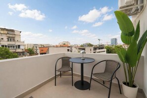 Ein Balkon mit zwei Korbstühlen, einem kleinen runden Tisch, einer Topfpflanze und Blick auf die Stadt.