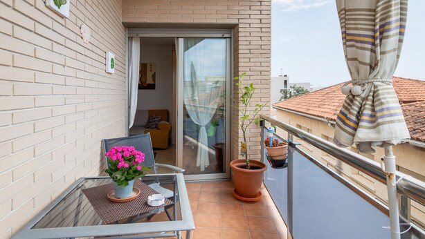 Ein Balkon mit Tisch, Stuhl, Topfpflanze und einer Schiebetür zu einem Innenraum.