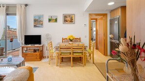 Ein Wohnzimmer mit Fernseher, Esstisch, Stühlen, einer Couch und einem Balkon mit Blick.