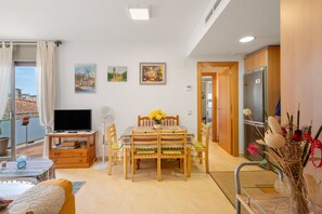 A living room with a TV, dining table, chairs, a sofa, and a balcony with a view. - Apartment 'Cubelles' with Sea Views, Private Terrace, and Air Conditioning (Cubelles)