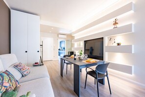 Ein modernes Wohnzimmer mit einer Couch, einem Esstisch mit Stühlen und einer Küche im Hintergrund.