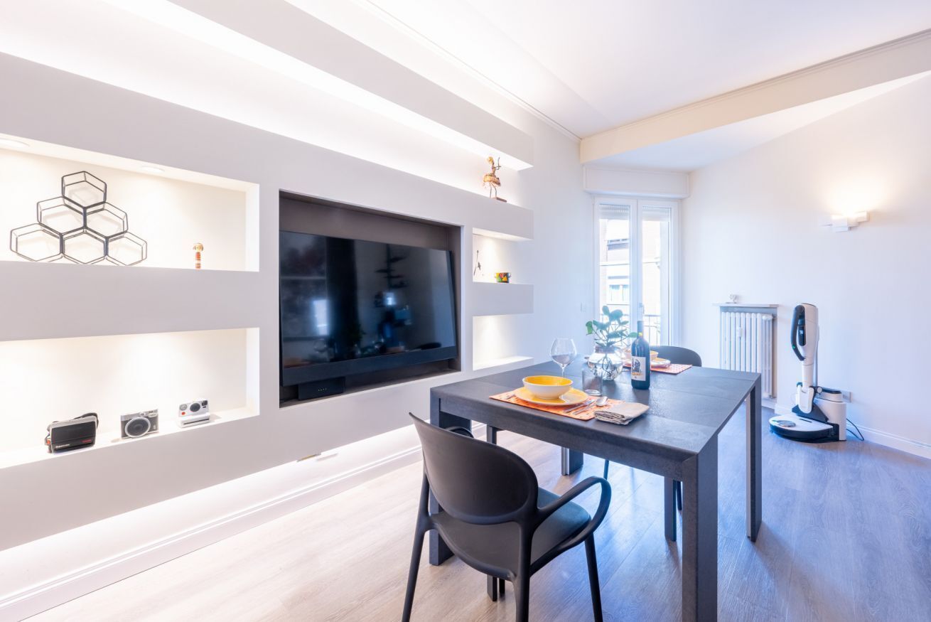 Un espace repas moderne doté d’un téléviseur à écran plat, d’une table avec des chaises et d’un coin cuisine équipé d’un robot pâtissier.