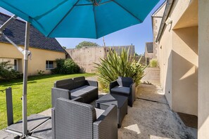 An outdoor patio with wicker furniture, a blue umbrella, and a concrete wall. - Holiday Home 'Gîte Aber 3km Plages' with Private Terrace, Garden & Wi-Fi (Telgruc-sur-Mer)