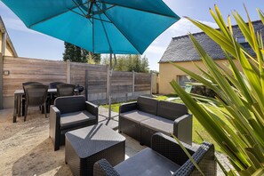 An outdoor patio with wicker furniture, a blue umbrella, and a wooden fence. - Holiday Home 'Gîte Aber 3km Plages' with Private Terrace, Garden & Wi-Fi (Telgruc-sur-Mer)