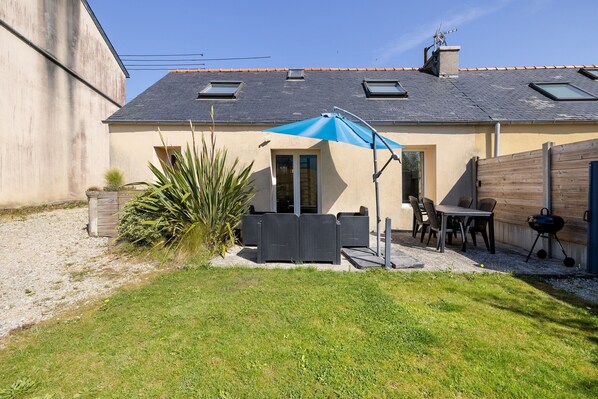 A house with a patio, outdoor furniture, a barbecue, and a large umbrella. - Holiday Home 'Gîte Aber 3km Plages' with Private Terrace, Garden & Wi-Fi (Telgruc-sur-Mer)