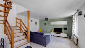 Uma sala de estar com escada de madeira, sofá, televisão e radiador.