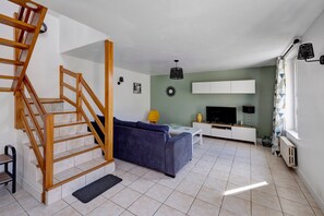 A living room with a wooden staircase, a sofa, a TV, and a radiator. - Holiday Home 'Gîte Aber 3km Plages' with Private Terrace, Garden & Wi-Fi (Telgruc-sur-Mer)