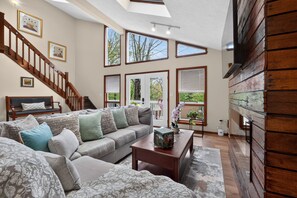 A spacious living room with a large sofa, a coffee table, and a staircase leading to an upper level.