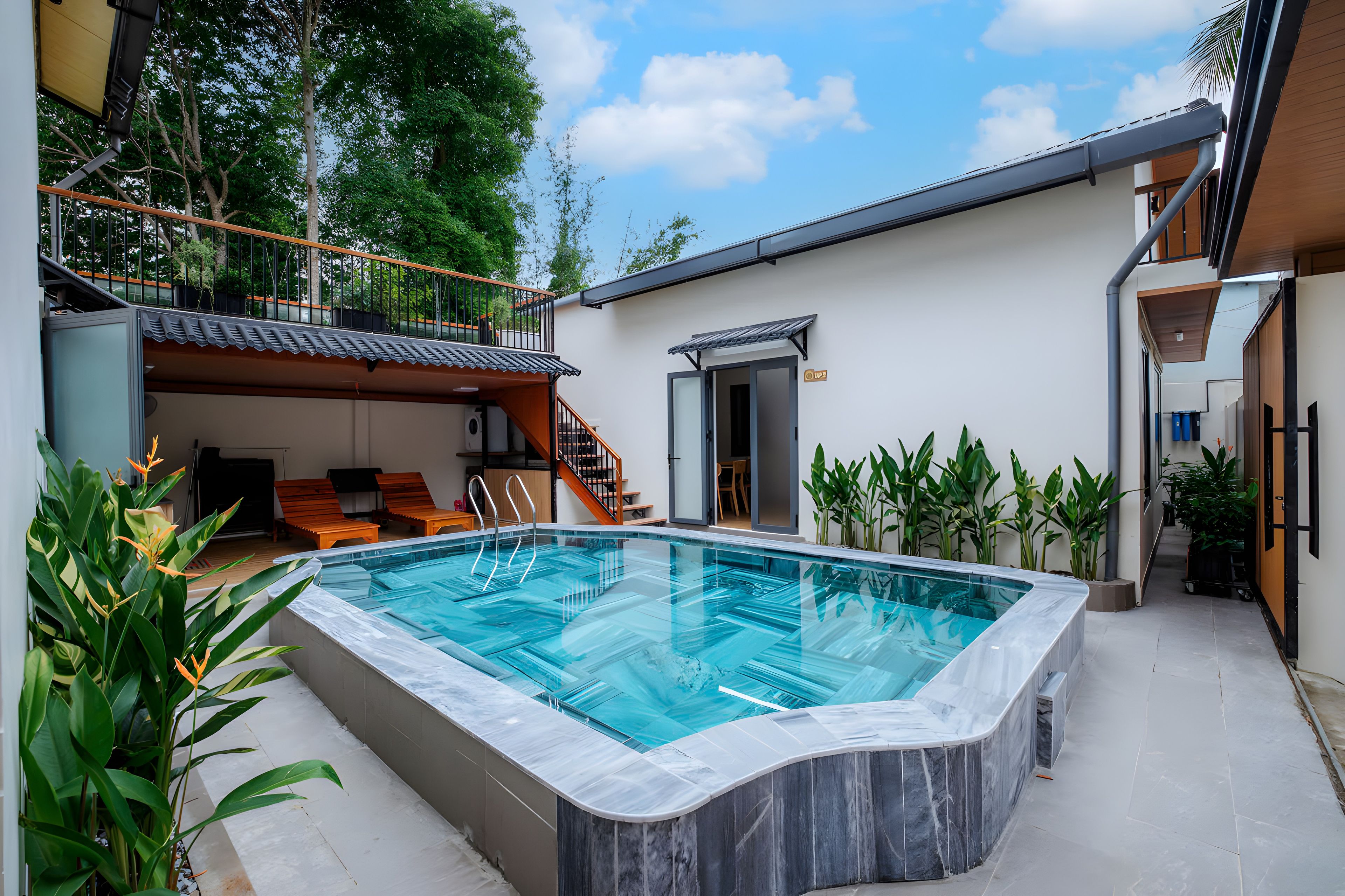 Una piscina con borde curvo, rodeada por un patio con mobiliario exterior y plantas en macetas.