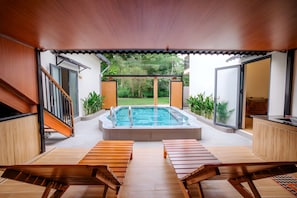 Un área de piscina moderna al aire libre con terraza de madera, sillas de descanso y un jacuzzi.