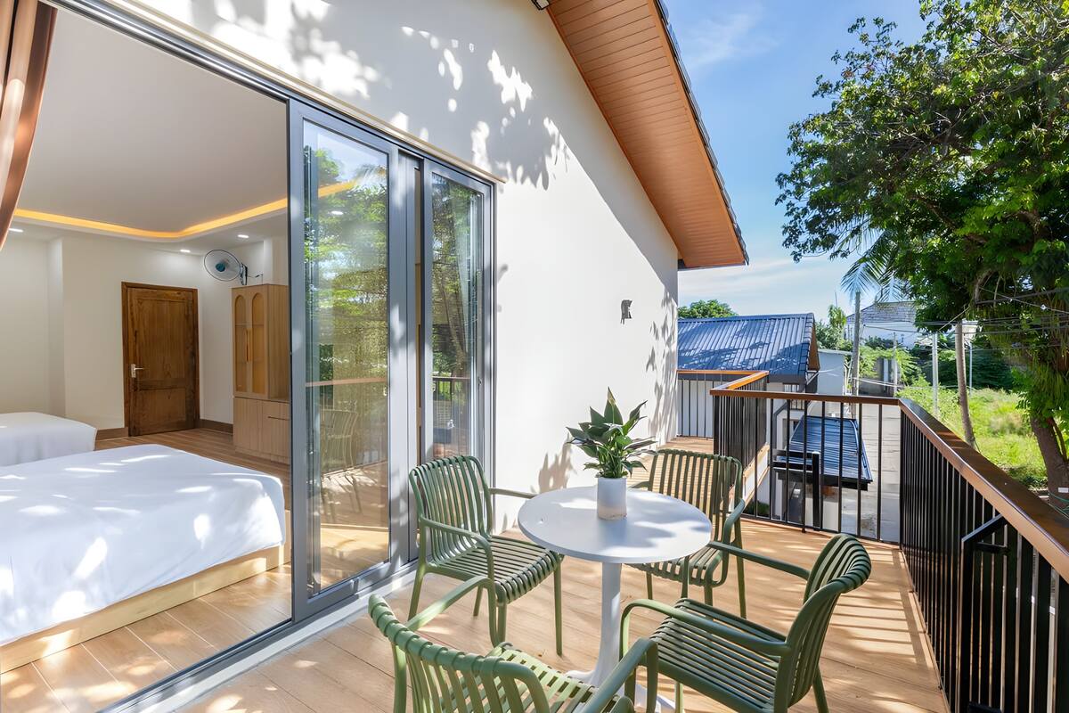 A modern room with a bed, a glass door leading to an outdoor area with a table and chairs, and a view of the outside.