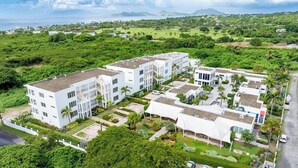 A modern hotel complex with multiple buildings, surrounded by lush greenery and a view of the ocean. - Belmont Villas (Vaughans)