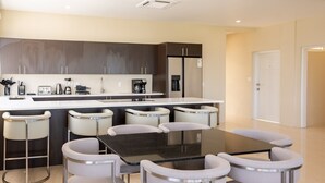 A modern kitchen with dark cabinets, a central island, and bar stools. - Belmont Villas (Vaughans)