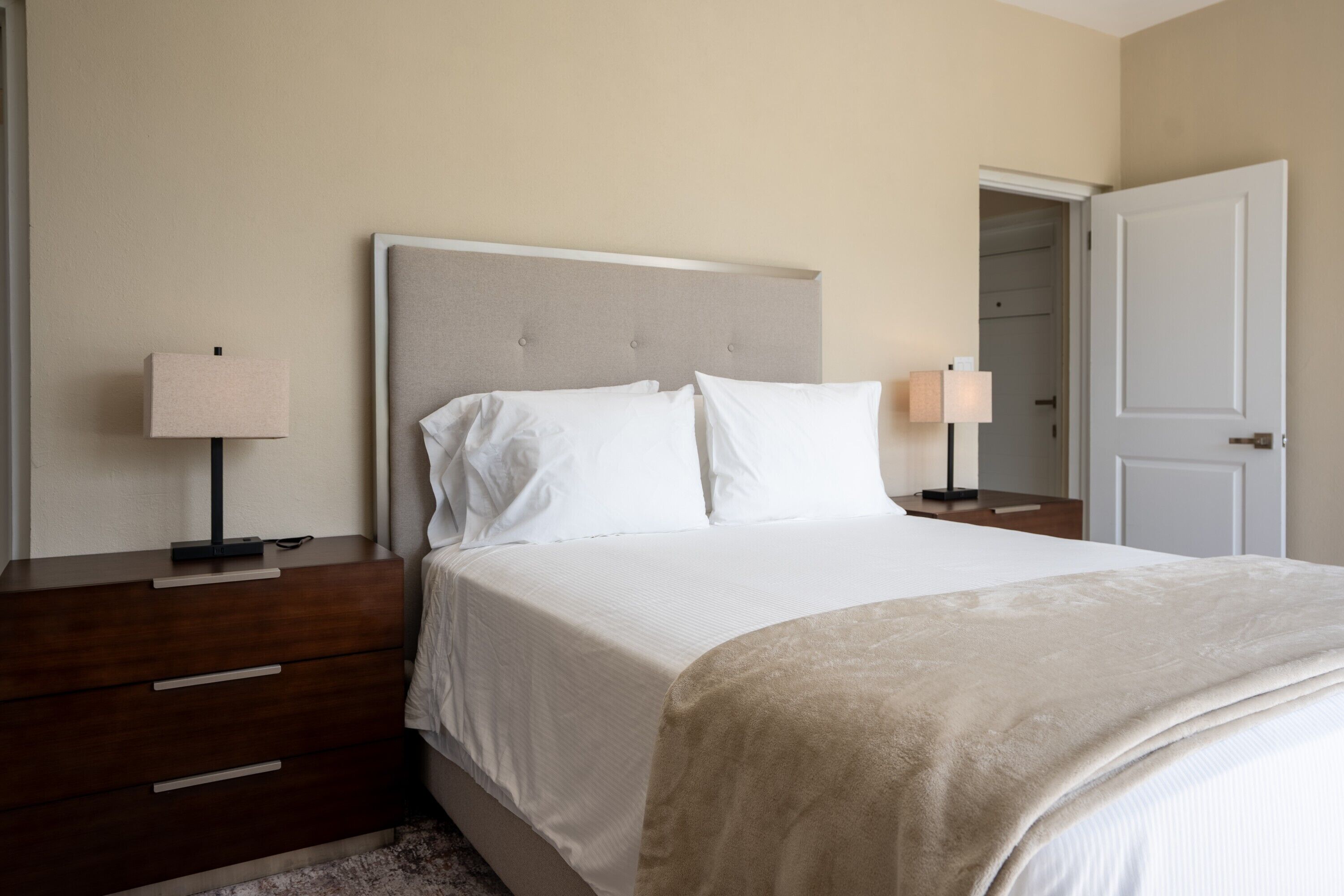 A bedroom with a bed, bedside tables, a nightstand, a door, and a lamp.