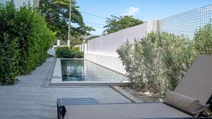 A pool with a concrete edge, a lounge chair, and a white wall with a metal fence. - Belmont Villas (Vaughans)