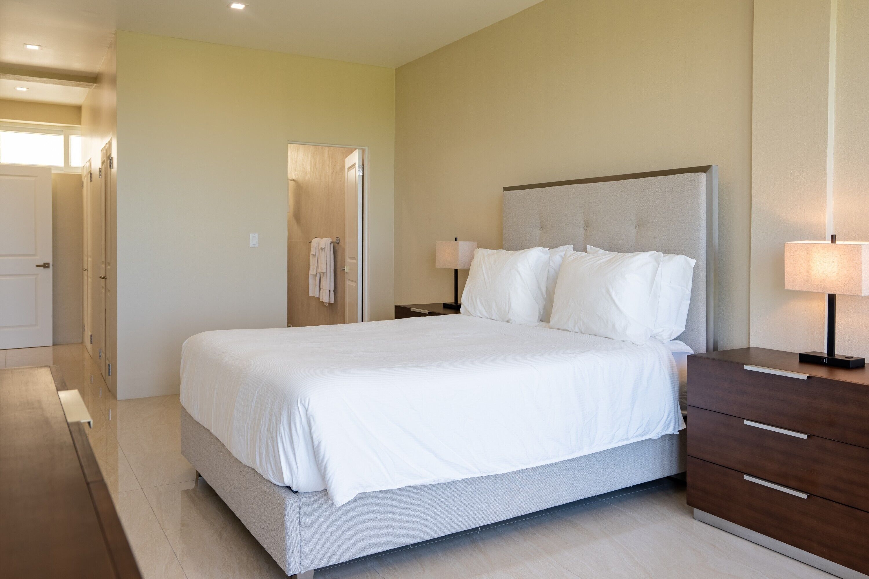 A hotel room with a large bed, bedside tables, a wardrobe, and a bathroom visible through an open door.