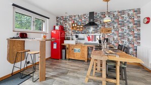 Une cuisine de taille réduite avec une table en bois, des tabourets de bar, un réfrigérateur rouge et un mur orné d’un motif.