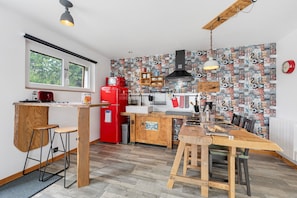 Une cuisine de taille réduite avec une table en bois, des tabourets de bar, un réfrigérateur rouge et un mur orné d’un motif.